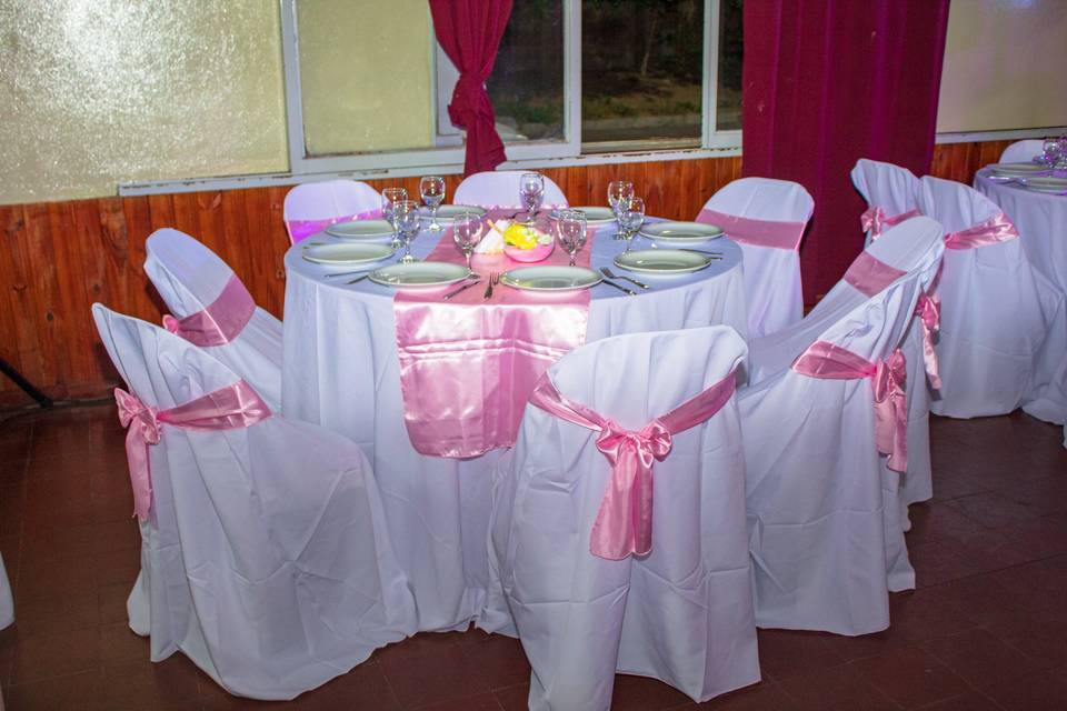 Mesa redonda con sillas vestidas de blanco y moño rosa