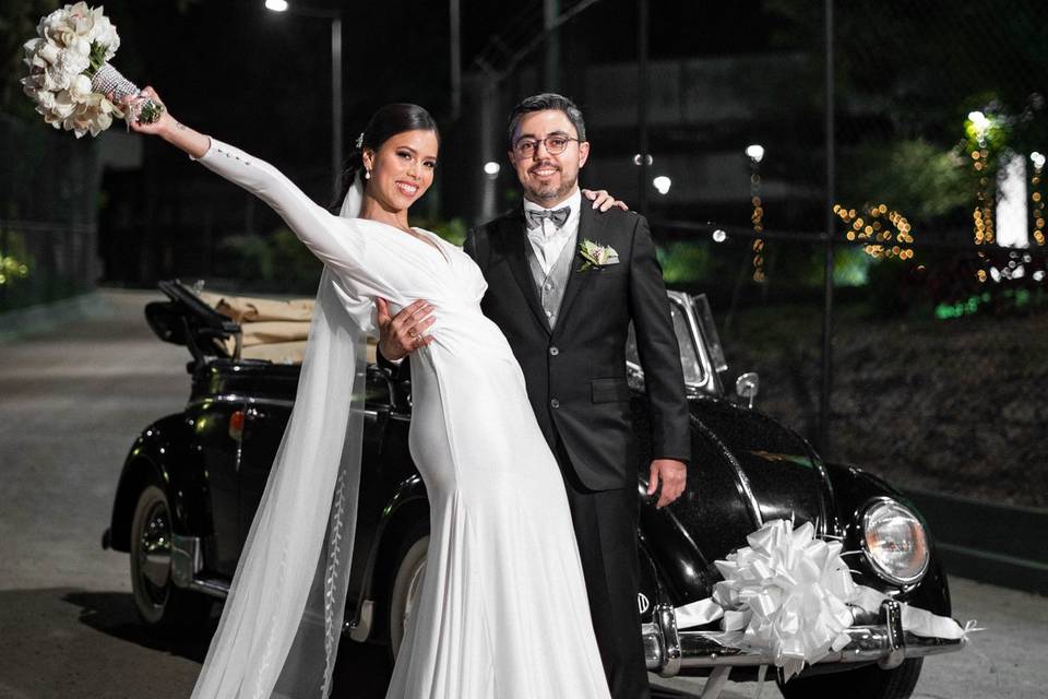 Novia y novio posando en la calle junto a un auto