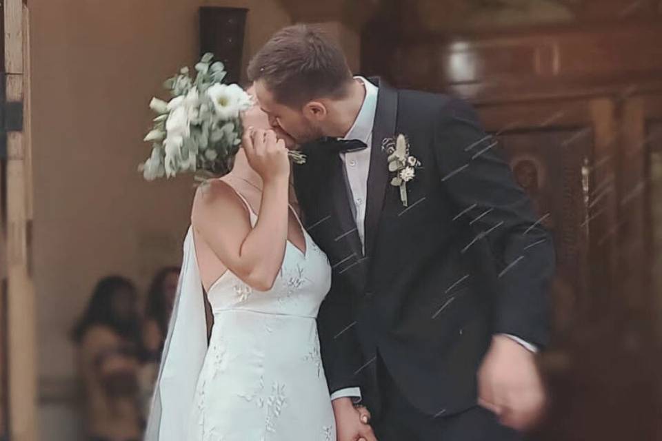 Novios besándose mientas novia se tapa la cara con su ramo