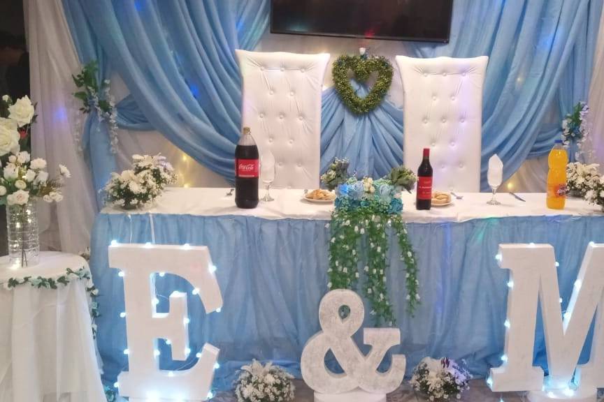 Mesa de novios con manteles azules y letras gigantes blancas